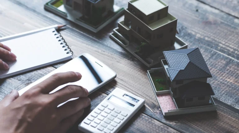 Person using a calculator and laptop to calculate home budget with financial documents on the table