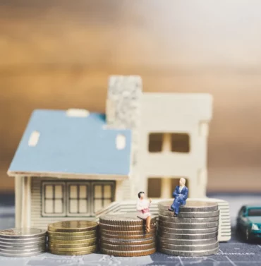 Miniature figures of people sitting on stacked coins symbolizing financial planning and economic inequality