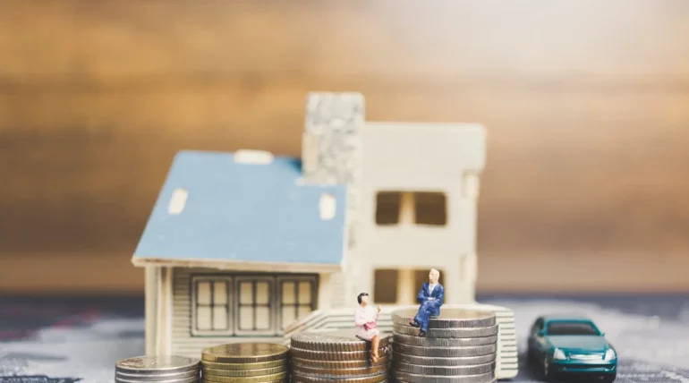 Miniature figures of people sitting on stacked coins symbolizing financial planning and economic inequality