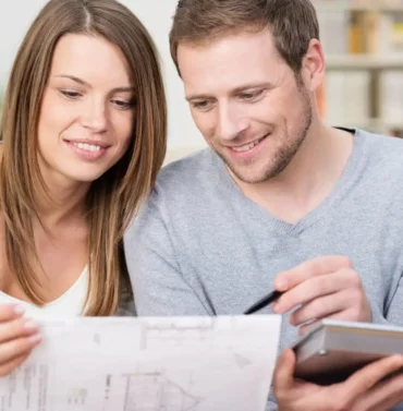 Young couple reviewing blueprints and discussing plans for their new home at a kitchen table