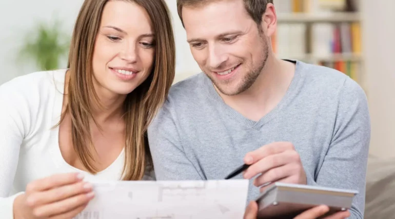 Young couple reviewing blueprints and discussing plans for their new home at a kitchen table