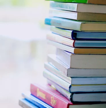 Selective focus image of a pile of assorted books with various titles stacked on a wooden surface