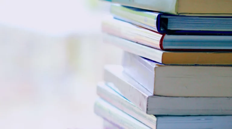 Selective focus image of a pile of assorted books with various titles stacked on a wooden surface